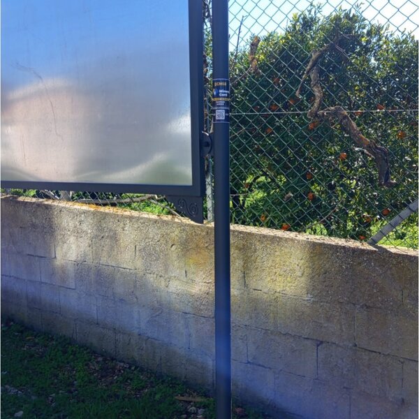 Cartello vuoto su palo davanti a muro e rete con piante sullo sfondo