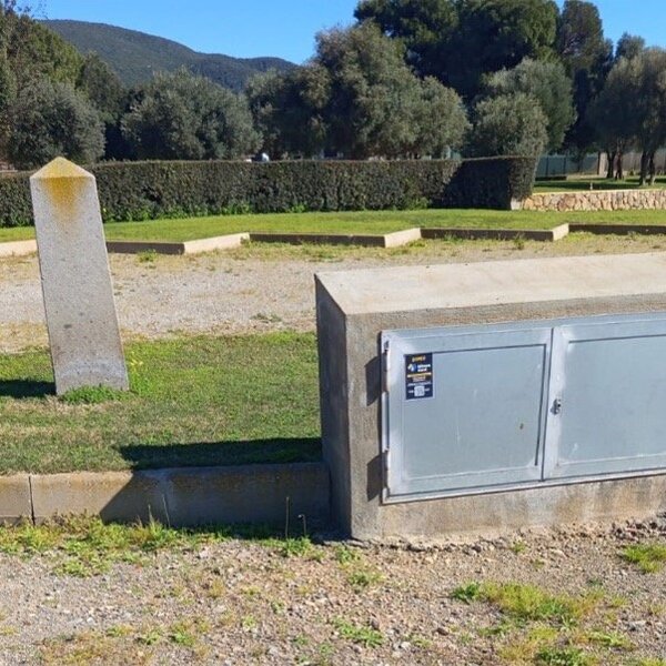 Contatore elettrico esterno in area verde con alberi e colline sullo sfondo