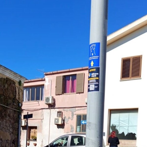 Segnale turistico su palo in strada con edifici e persona sullo sfondo
