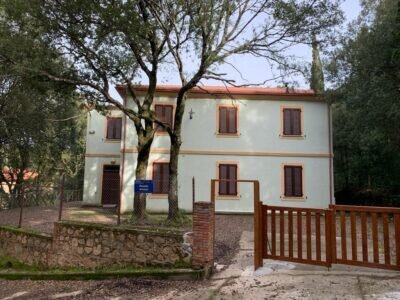 Maison blanche à deux étages avec fenêtres marron et portail en bois ouvert