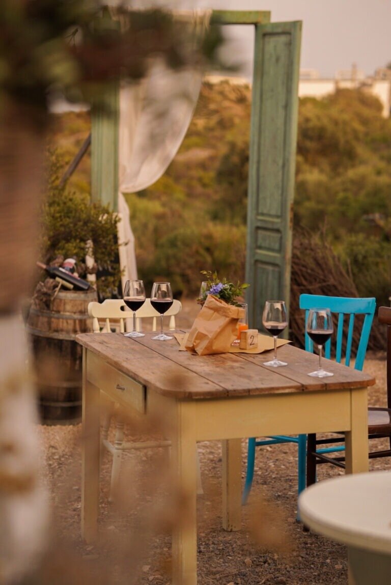 Rustic outdoor table with wine glasses and flowers in a paper bag