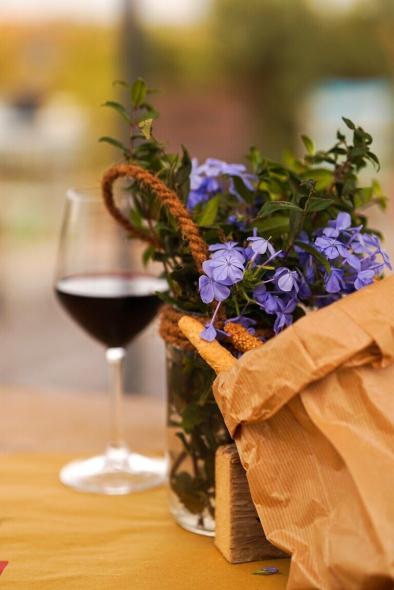Glass of red wine, purple flowers, and bread in a paper bag