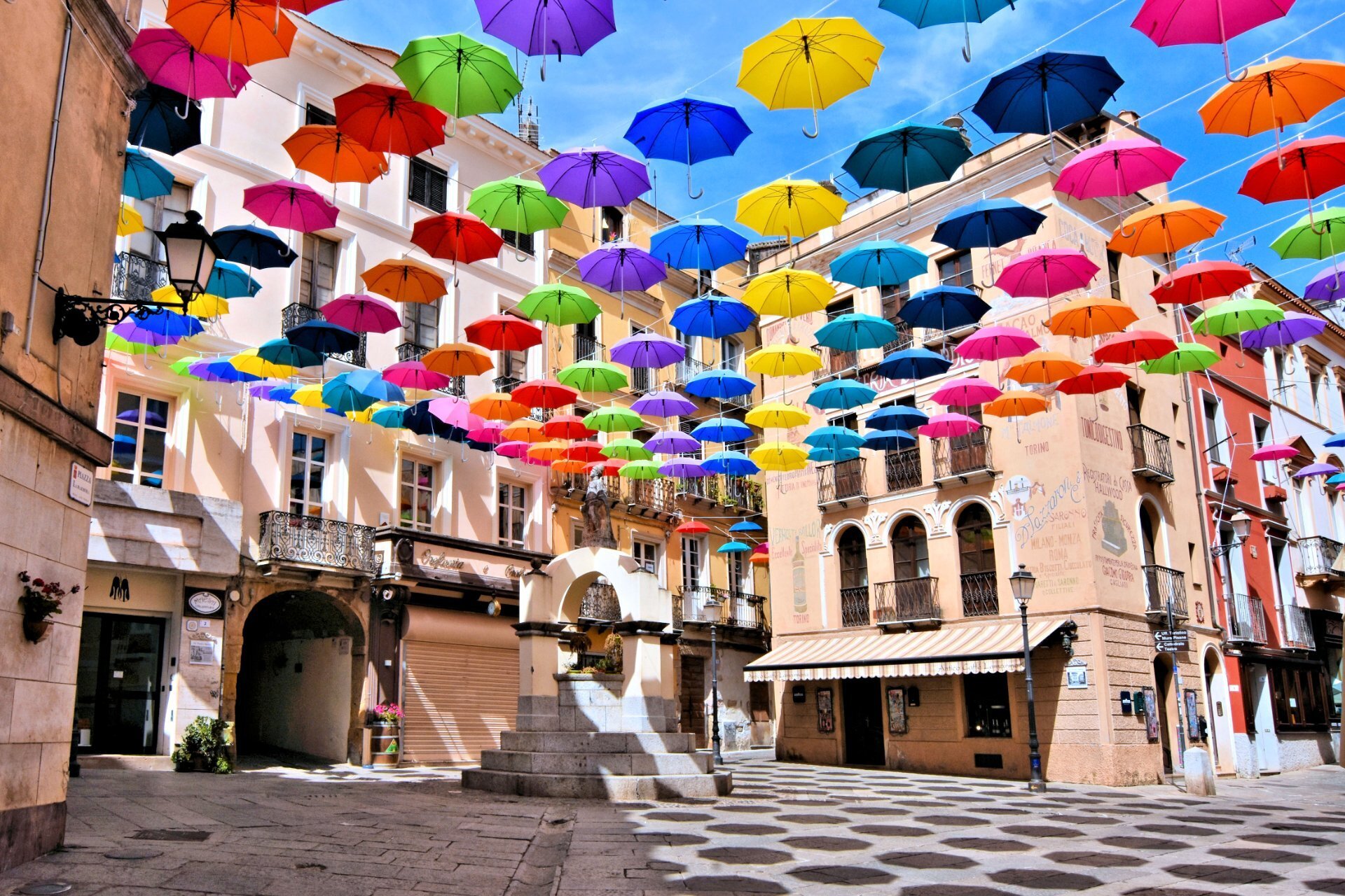 Ombrelli colorati sospesi sopra una piazza storica soleggiata.