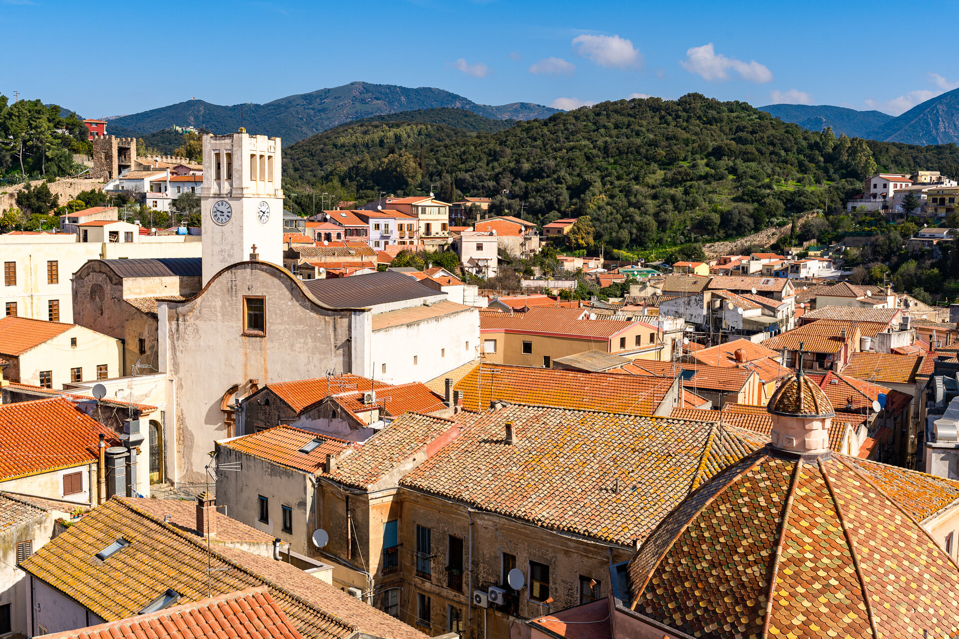 Veduta del centro storico con tetti rossi e campanile, sullo sfondo colline verdi.