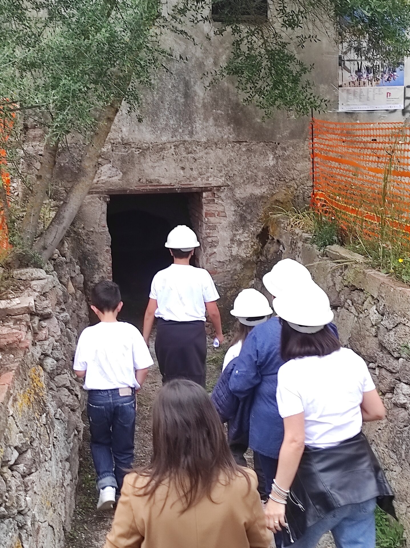 Gruppo di persone con caschi bianchi entra in una grotta o miniera.