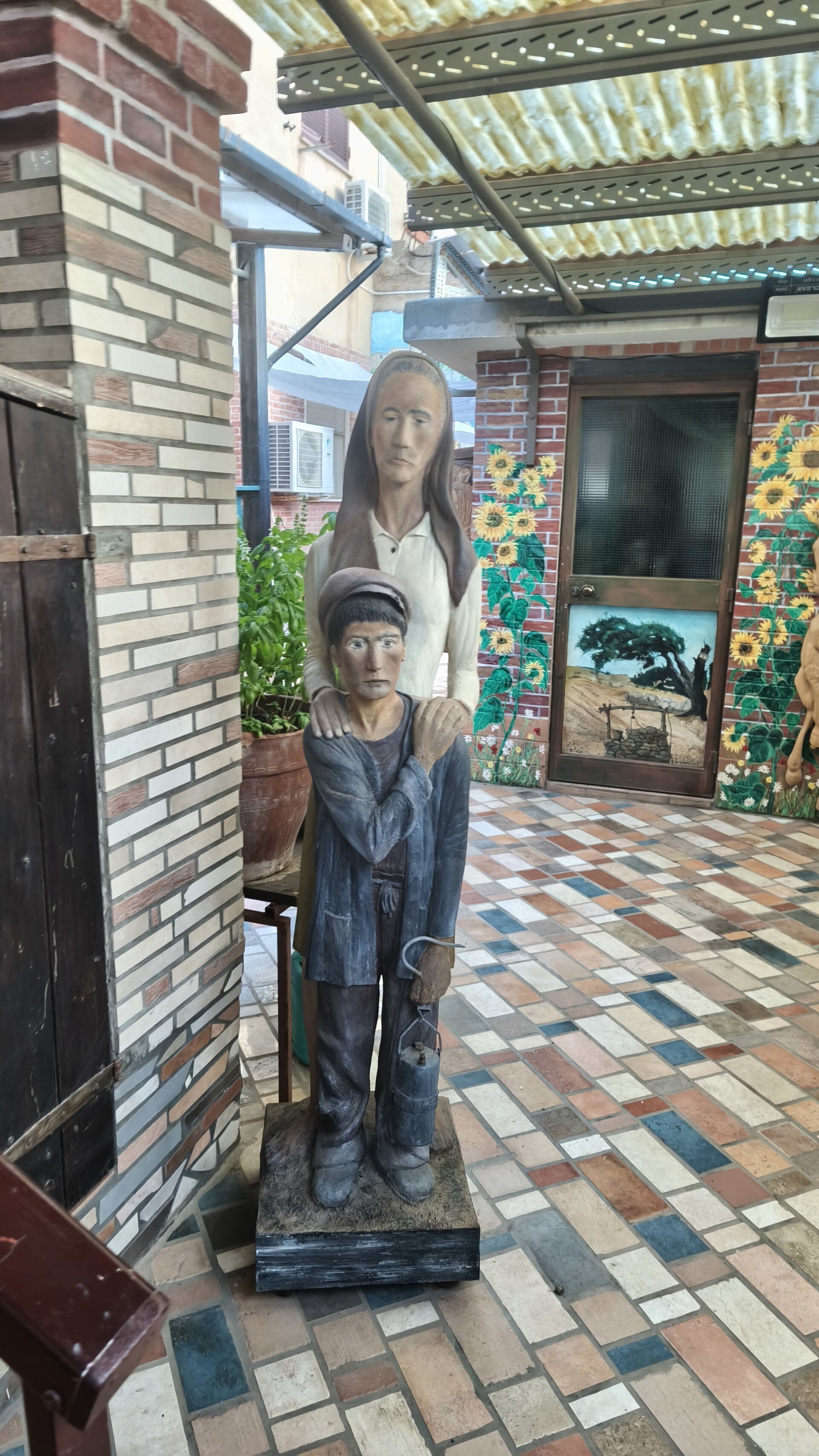 Statue di donna e bambino in cortile con pavimento a scacchi e murales di girasoli