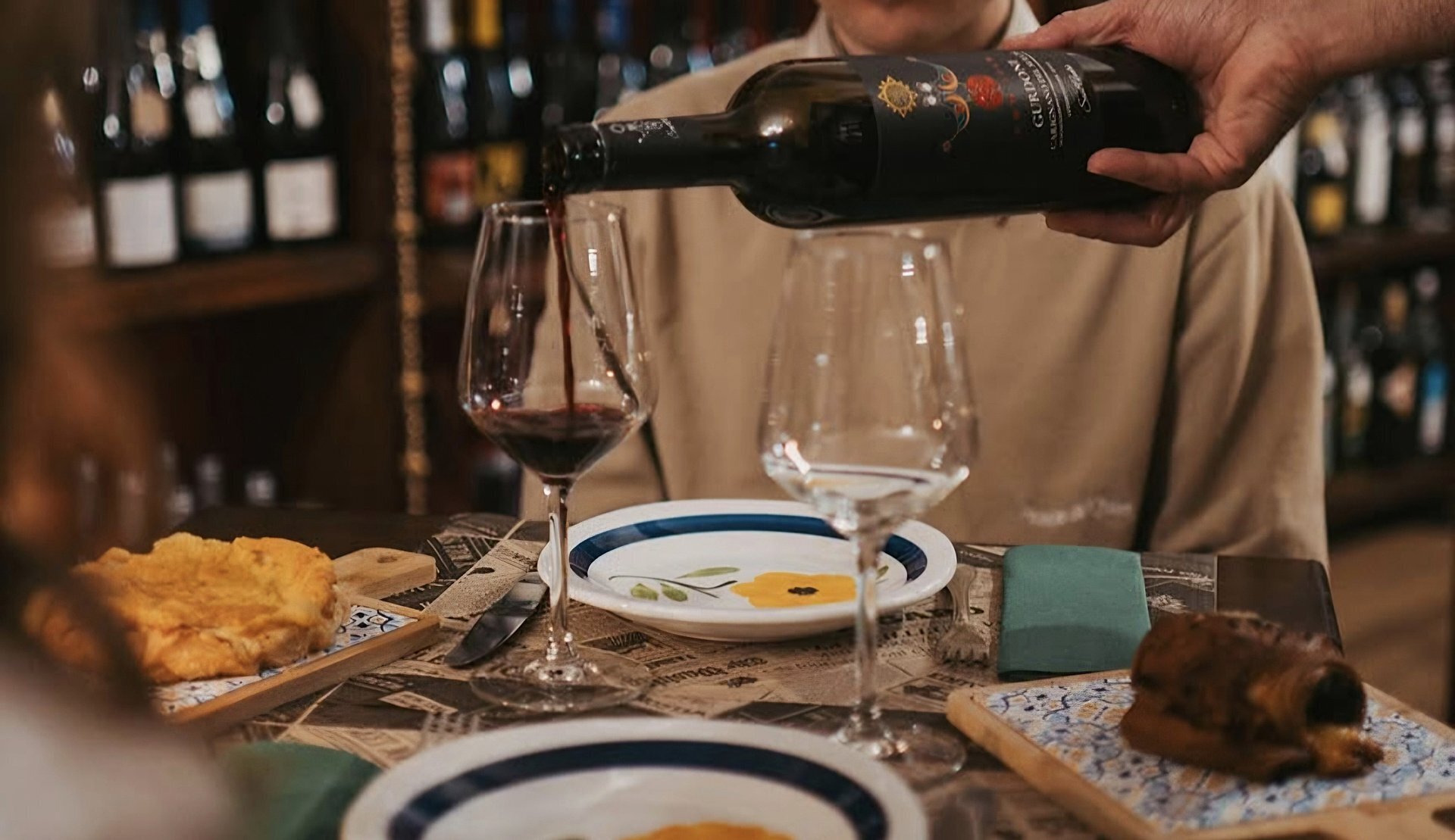 Red wine being poured into a glass at a set dining table.