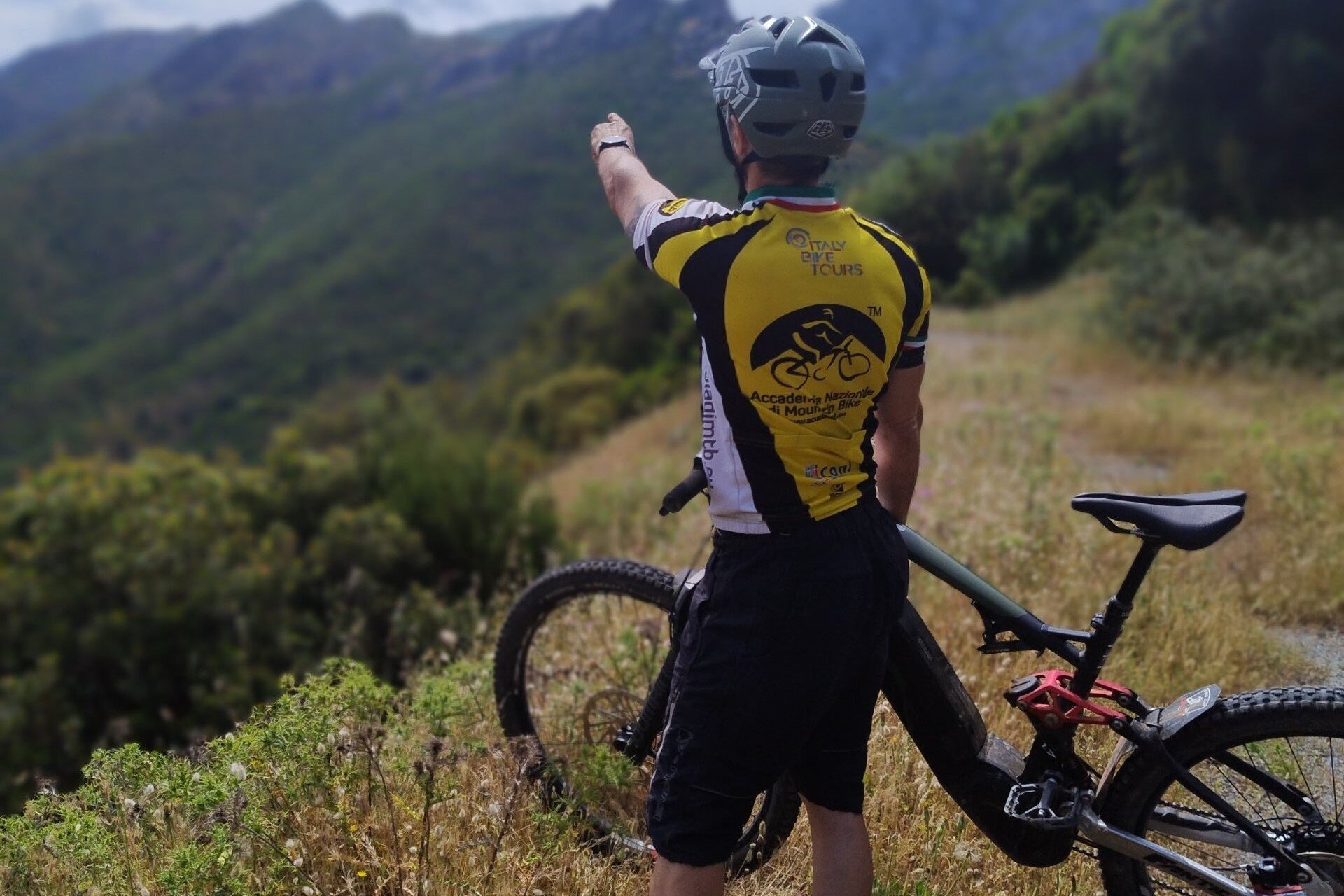 Cyclist wearing helmet points towards a mountain during a bike ride.