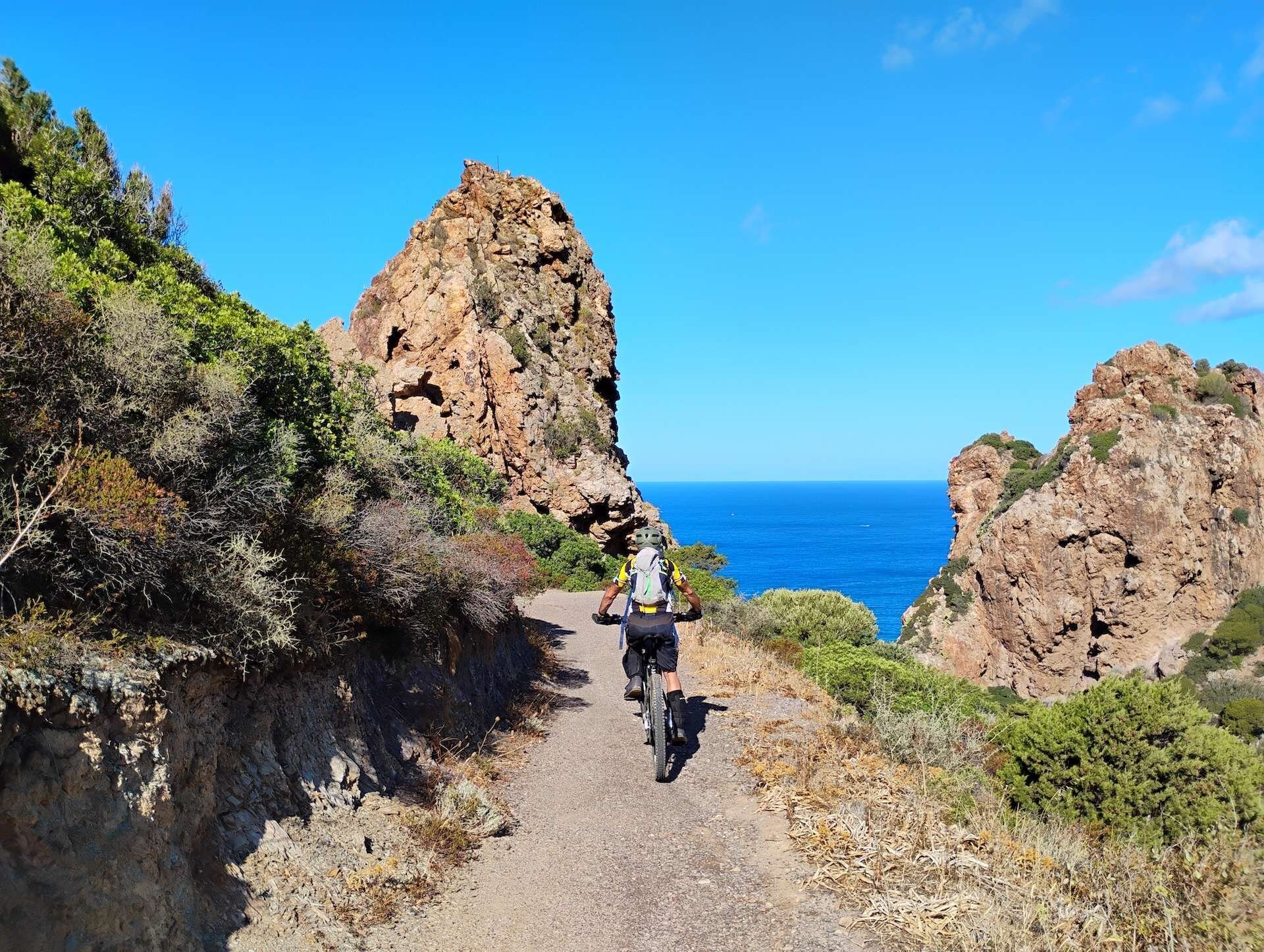 Cyclist on coastal path between rocks and blue sea under clear sky