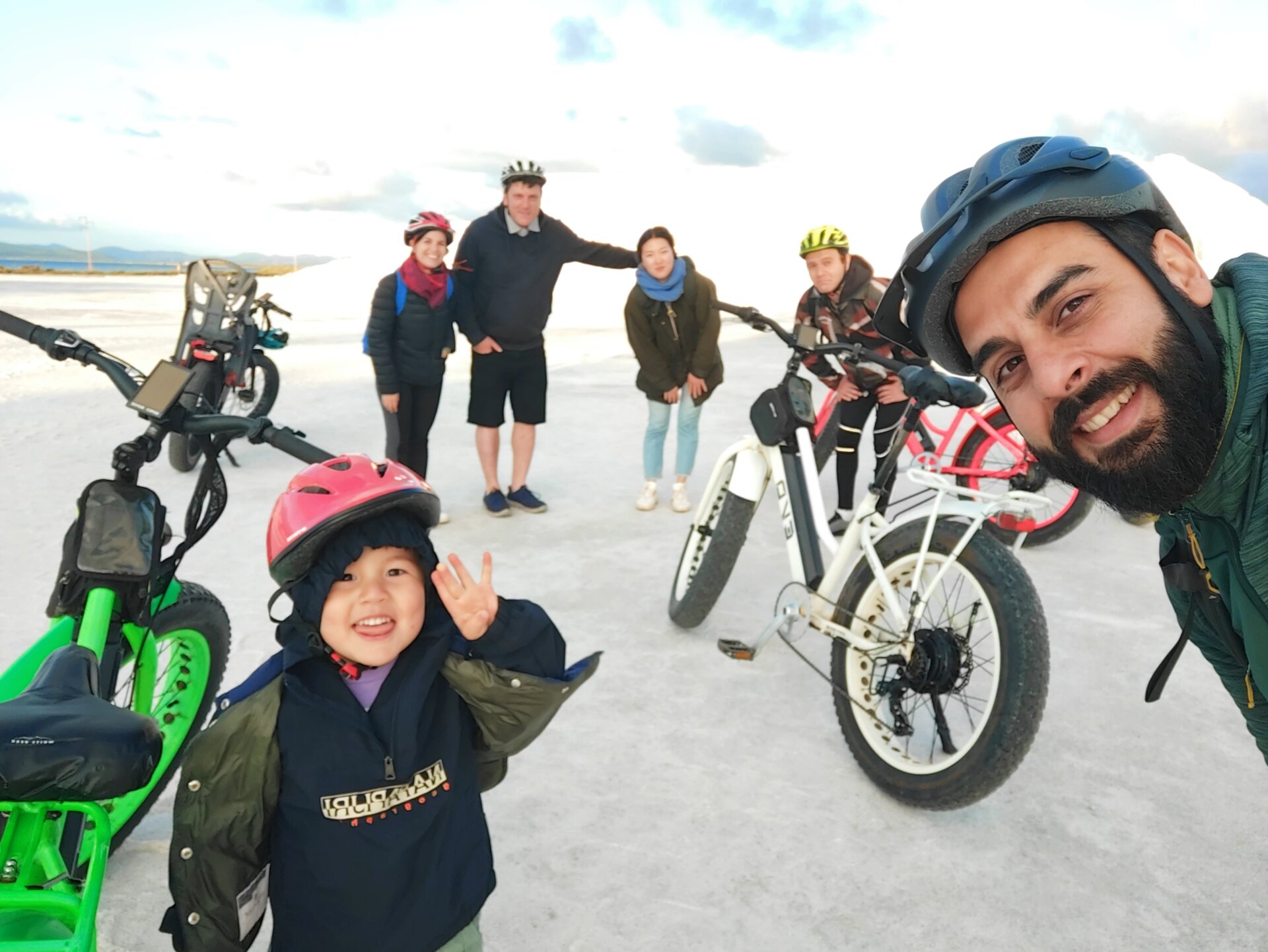 Group of people with electric bikes in an open area, smiling and wearing helmets.