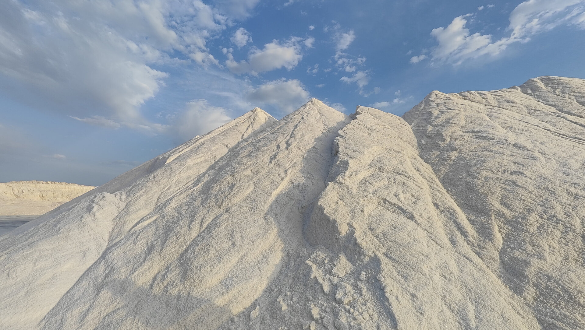 Piles of light sand under a blue sky with scattered clouds