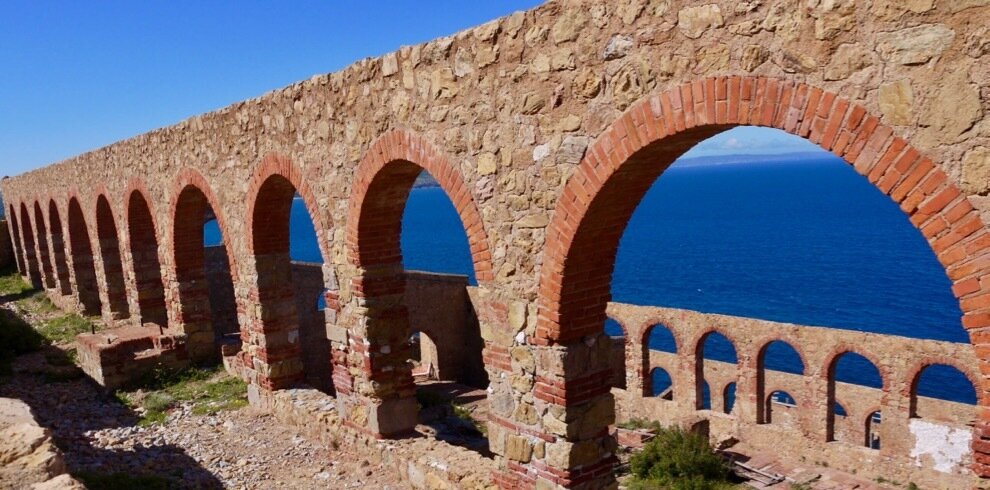 Ancient stone arches overlooking the blue sea under a clear sky.