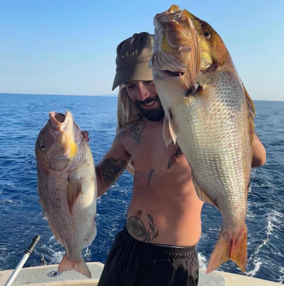 Uomo con cappello mostra due grandi pesci pescati in mare aperto