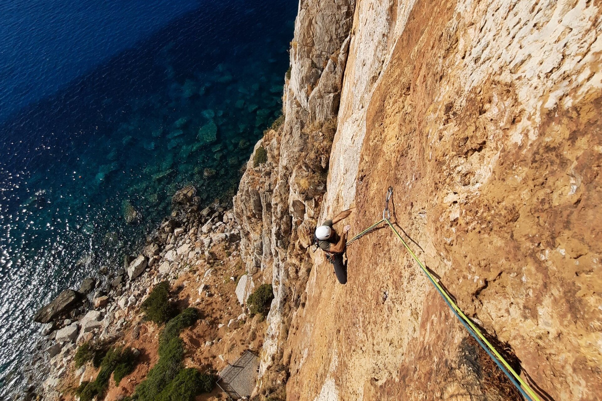 Climber on rocky cliff above clear blue sea.
