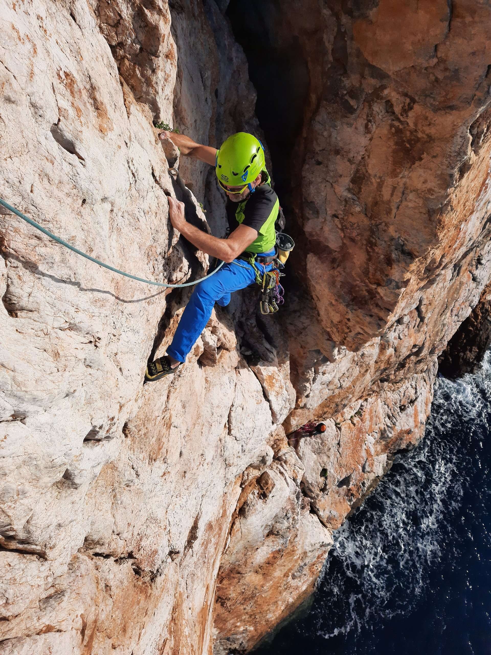 Climber with green helmet on rocky cliff above the sea