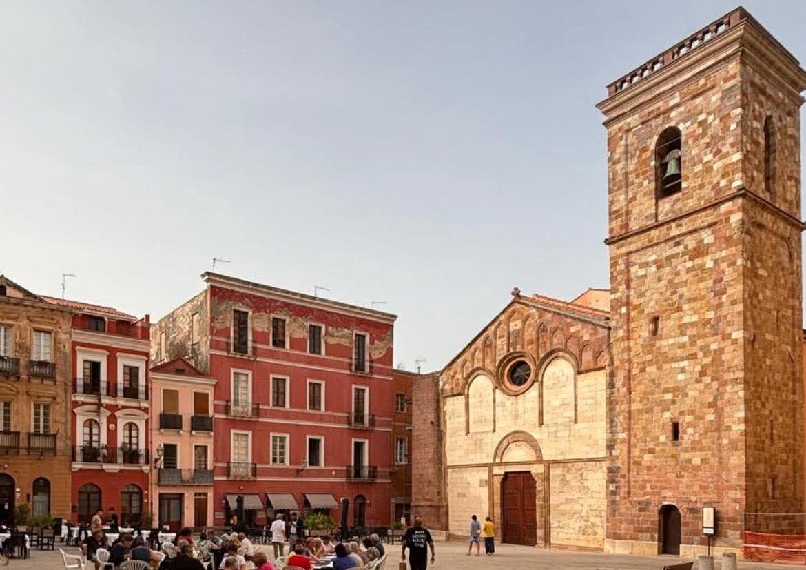 Square with seated people and historic stone and red brick buildings.