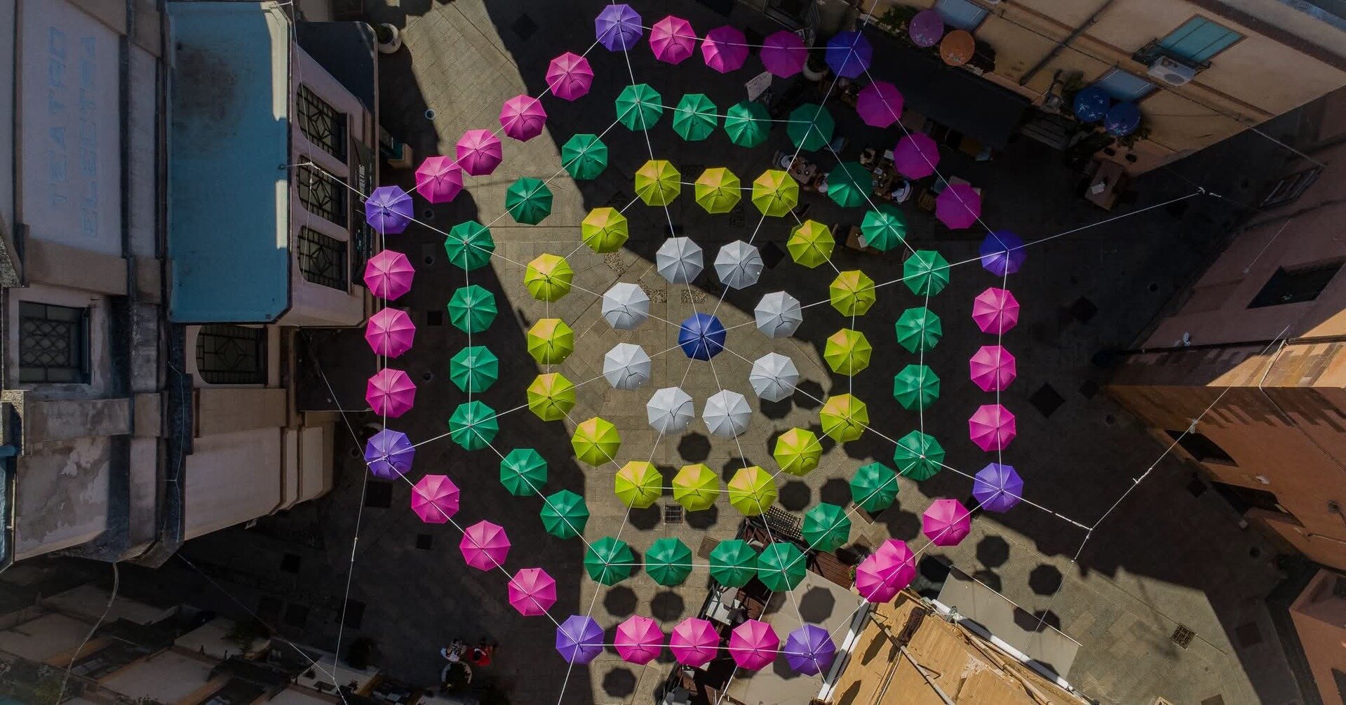 Colorful umbrellas suspended forming concentric circles in an urban space.