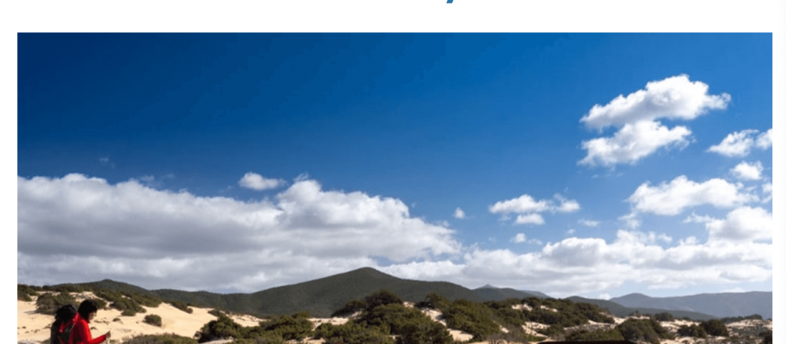 Natural landscape with sandy dunes, vegetation, and blue sky with white clouds