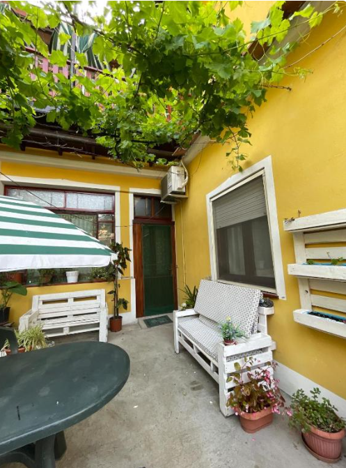 Cortile con pareti gialle, panchine bianche e piante verdi.