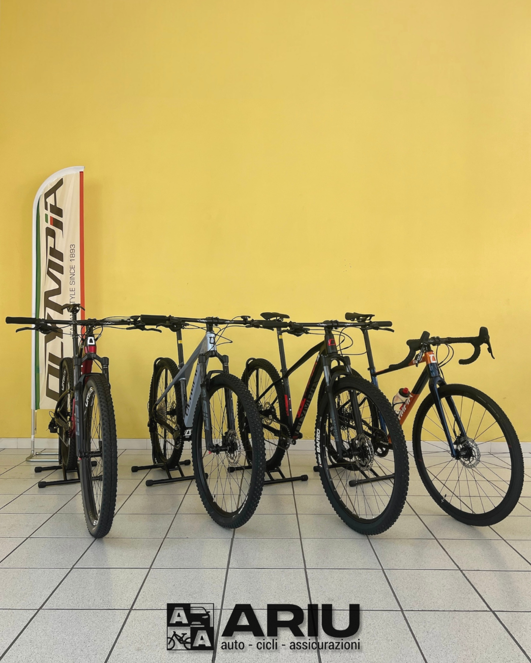 Four racing and mountain bikes displayed on tiled floor against yellow wall.