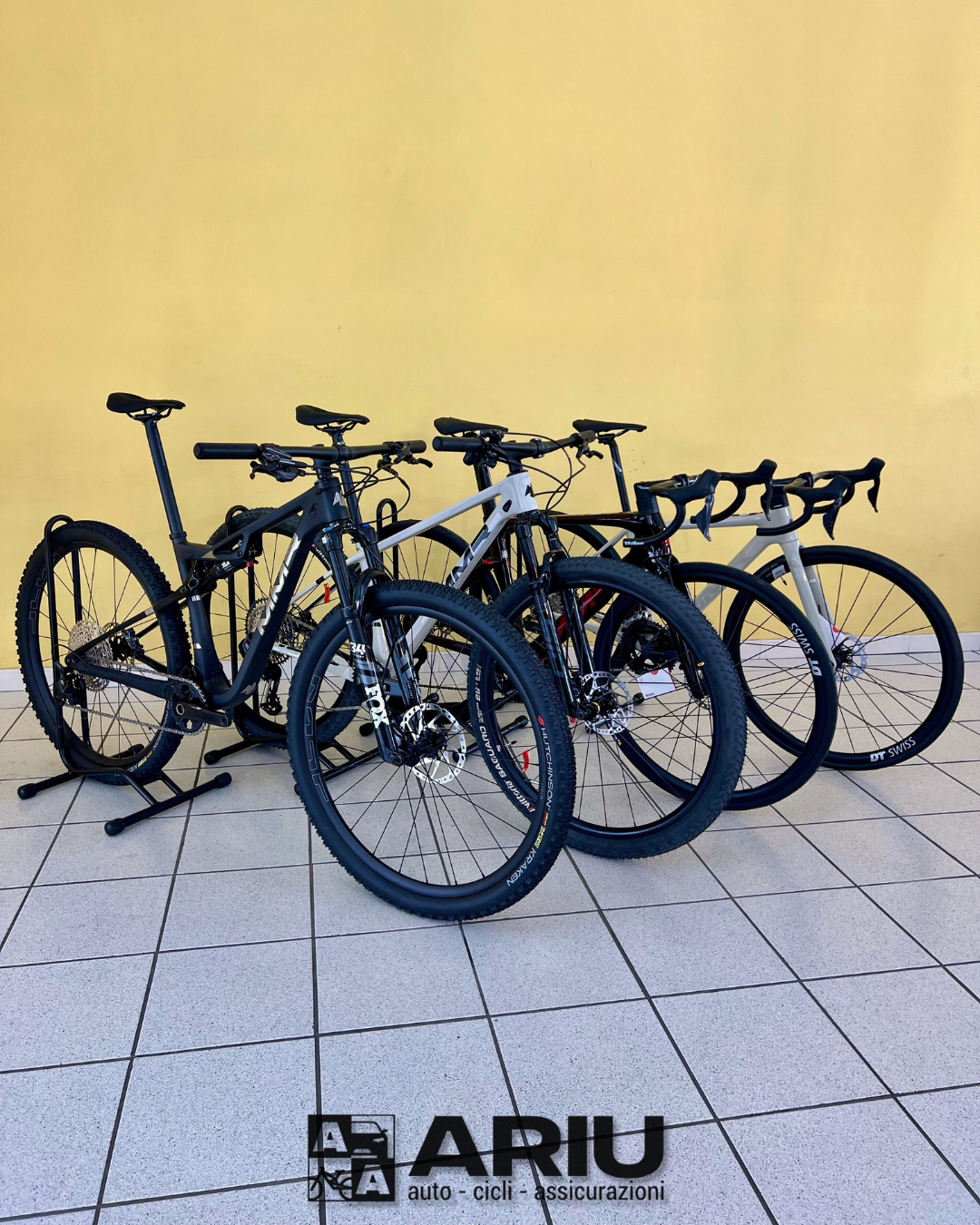Four road and mountain bikes on tiled floor with yellow wall background