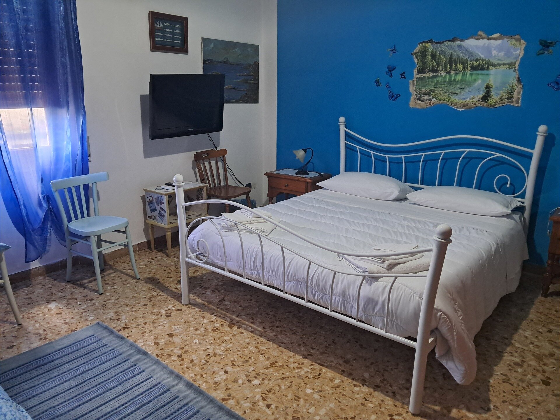 Camera da letto con letto matrimoniale, parete blu e televisore a muro.