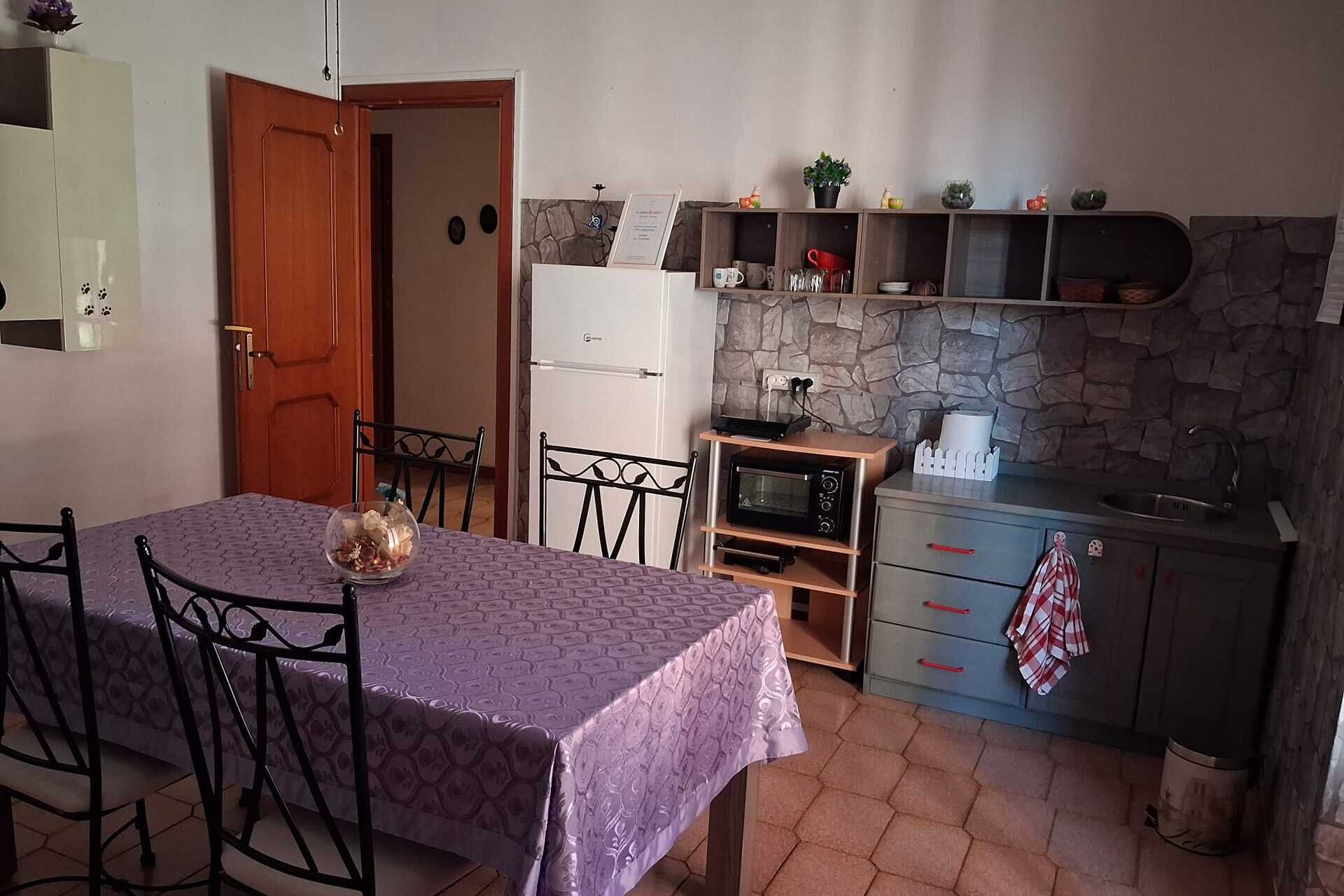 Cucina con tavolo coperto da tovaglia viola e sedie nere in ferro battuto.