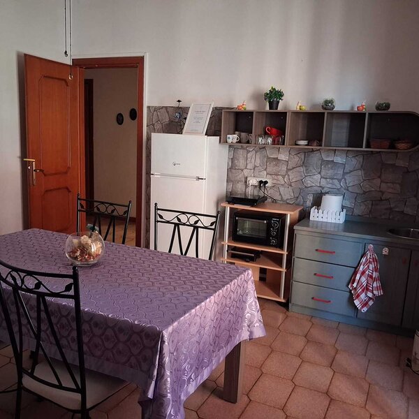 Kitchen with table covered by purple tablecloth and black wrought iron chairs.
