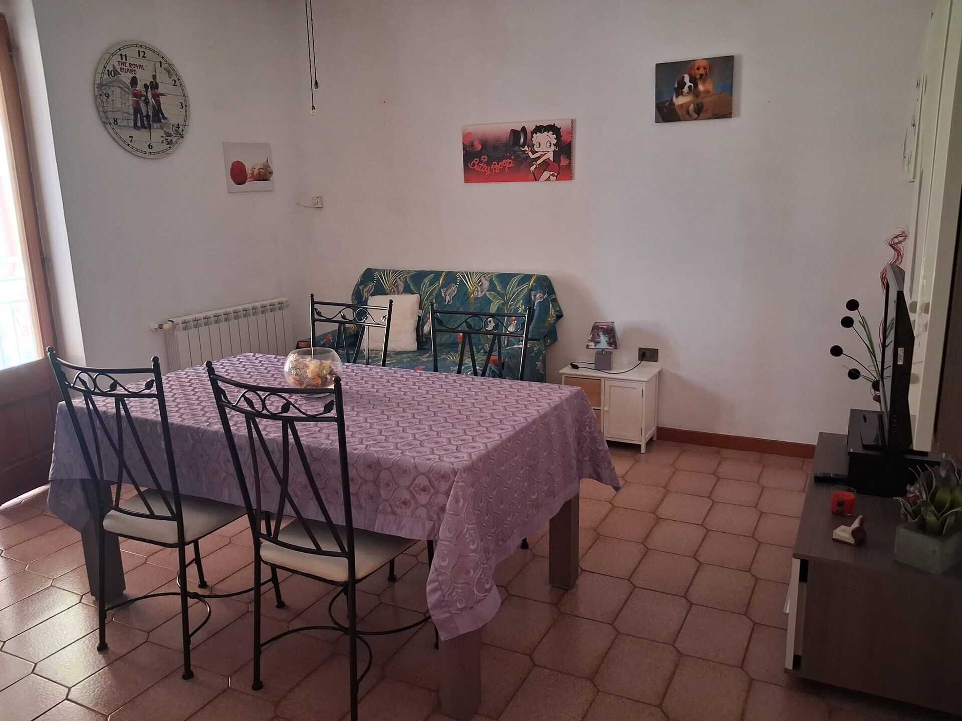 Sala da pranzo con tavolo coperto da tovaglia viola e sedie nere in ferro battuto