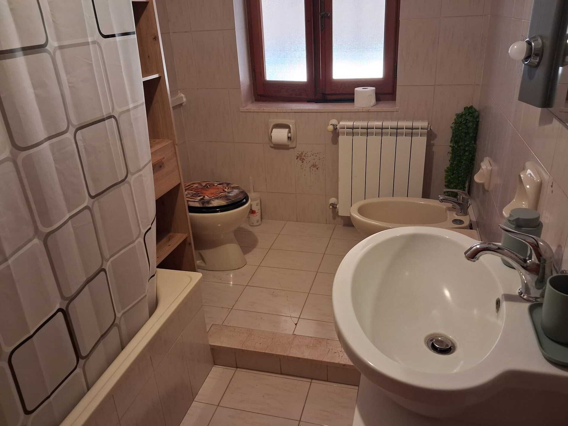 Bagno con lavabo, bidet, wc, vasca e finestra con tenda doccia.