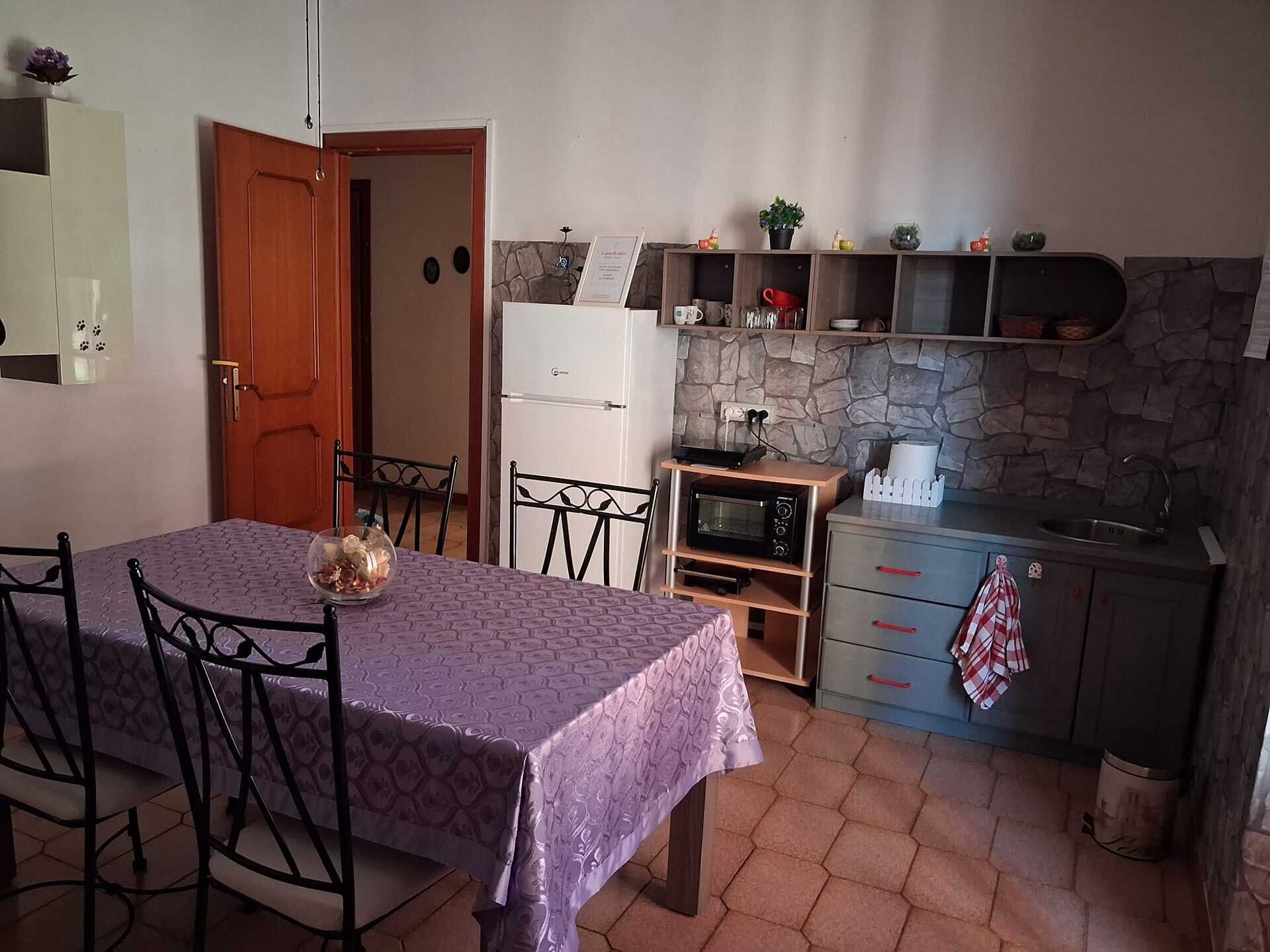 Cucina con tavolo coperto da tovaglia viola e sedie nere in ferro battuto.