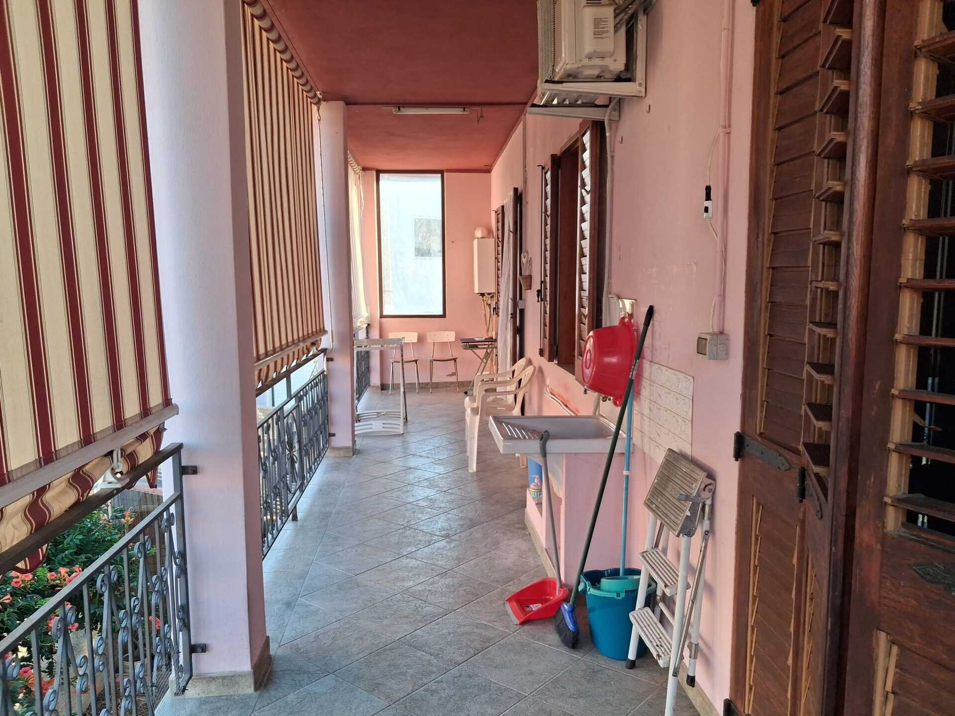 Balcone lungo con pavimento piastrellato e attrezzi per pulizia.