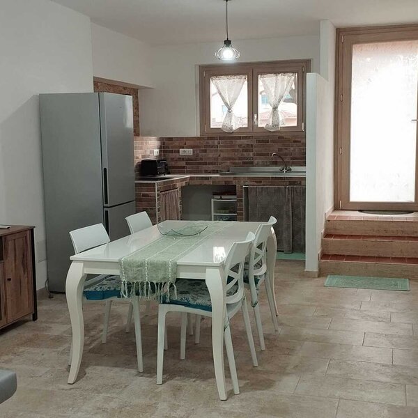 Cucina moderna con tavolo bianco e quattro sedie, frigorifero e finestra luminosa.