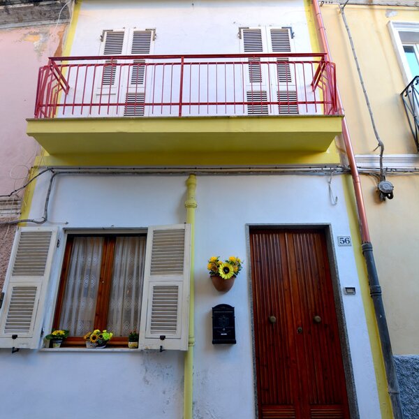 Facciata di casa con balcone rosso, porta in legno e fiori gialli