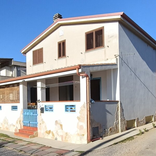 Casa bifamiliare con persiane marroni e cancello azzurro sotto cielo sereno