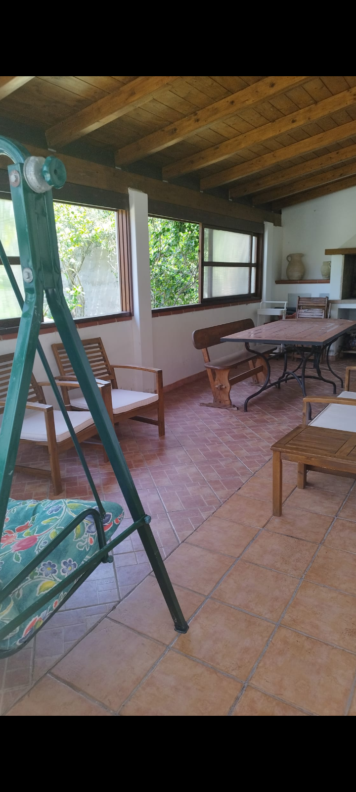 Veranda arredata con sedie, panca e tavolo in legno, pavimento piastrellato.