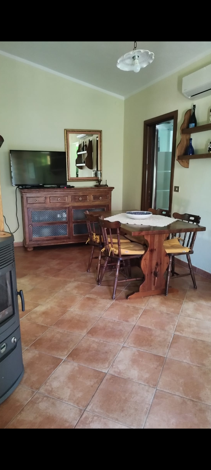Sala da pranzo rustica con tavolo in legno, sedie imbottite e mobile con TV.