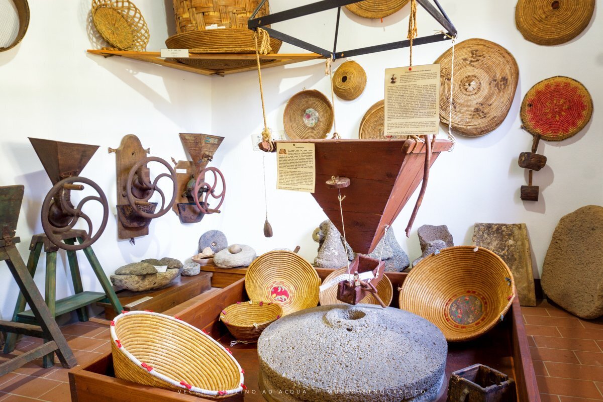 Interno di museo con antichi strumenti per la macinazione e cesti di paglia.