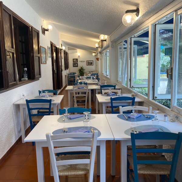 Sala ristorante con tavoli apparecchiati e sedie blu e bianche vicino a finestre aperte