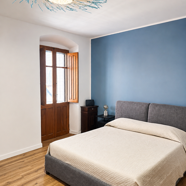 Camera da letto con letto matrimoniale, parete blu e porta finestra in legno aperta