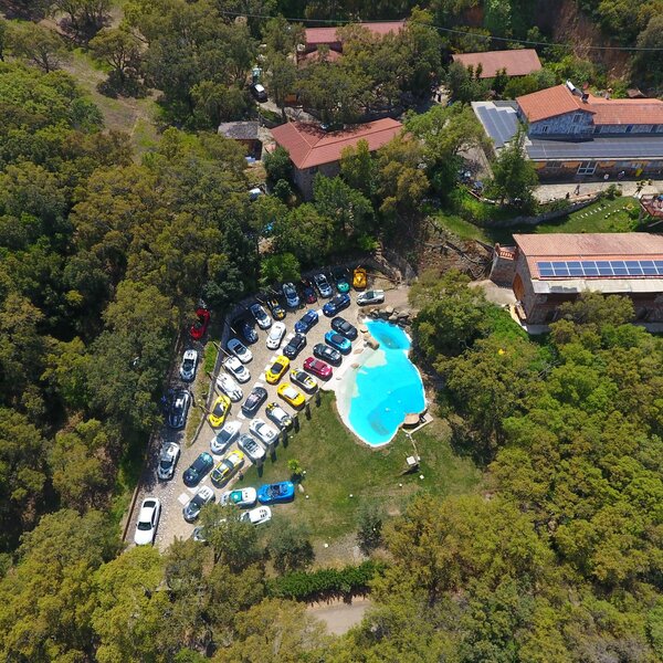Vista aerea di auto parcheggiate vicino a piscina e edifici immersi nel verde.