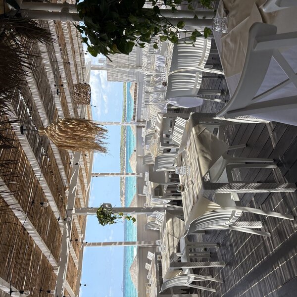 Ristorante all'aperto con vista sul mare e tavoli apparecchiati sotto pergolato di legno.