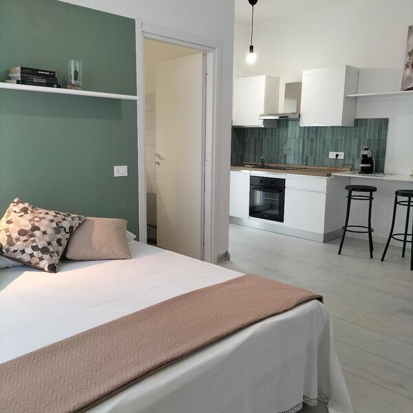 Camera con letto e cucina moderna adiacente, colori neutri e arredi minimalisti