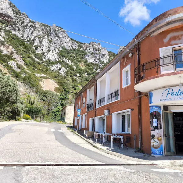 Ristorante con tavoli esterni vicino a una strada e montagne rocciose sullo sfondo