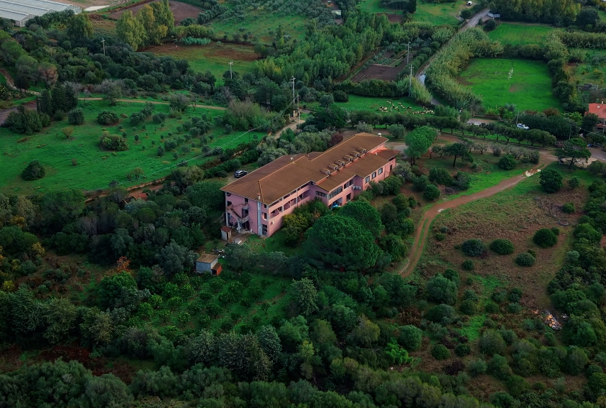 Vista aerea di un edificio rosa circondato da vegetazione e campi verdi.