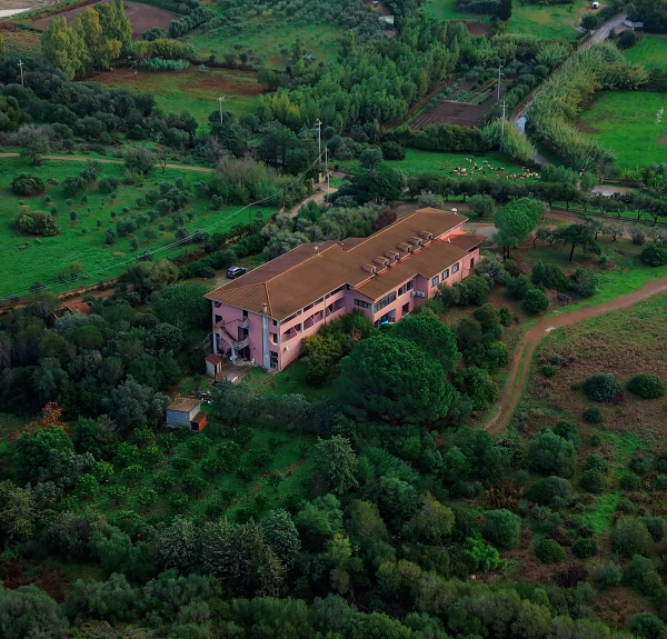 Aerial view of a pink building surrounded by greenery and green fields.