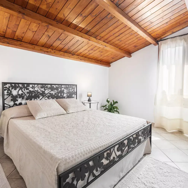 Schlafzimmer mit Doppelbett, Holzdecke und Fenster mit weißem Vorhang.