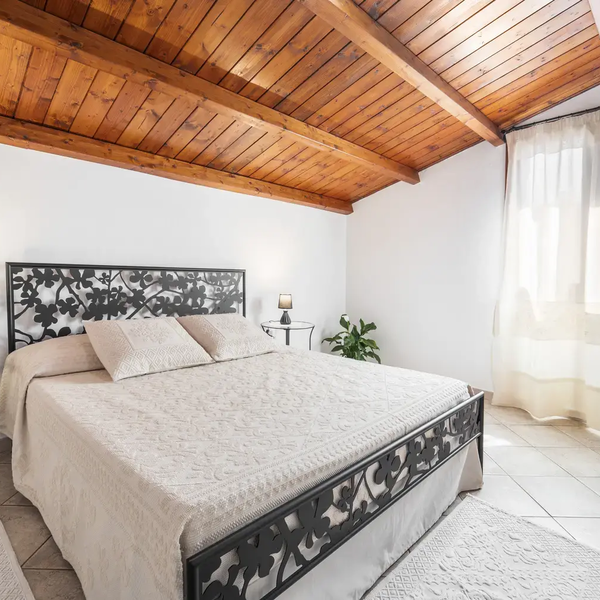 Camera da letto con letto matrimoniale, soffitto in legno e finestra con tenda bianca.