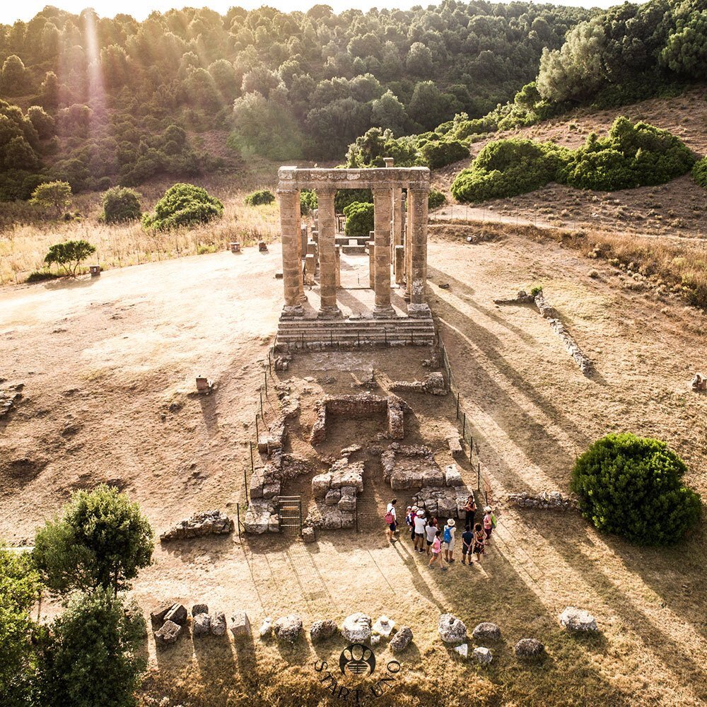 Rovine di un tempio antico con visitatori e alberi sullo sfondo al tramonto.